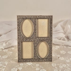 May include: A rectangular silver-toned metal picture frame featuring an intricate embossed floral and vine pattern. The frame contains four distinct openings for photographs: two oval-shaped apertures and two rectangular apertures arranged in a grid.