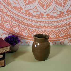 May include: A brown ceramic vase with a rounded body and a slightly flared lip. The vase is sitting on a light green surface.