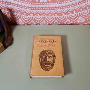 Peut inclure: Un livre relié de couleur beige intitulé "The Concise Oxford Dictionary of Quotations" avec une illustration brune d'un masque théâtral sur la couverture.