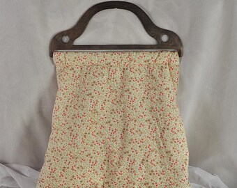 May include: A handmade tote bag with a wooden handle. The bag features a cream-colored fabric covered in a pattern of small red and brown floral designs. The wooden handle is a dark brown color.