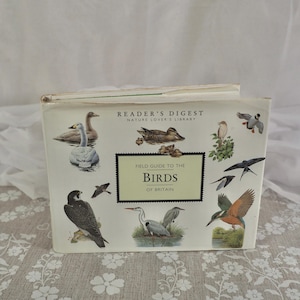 Op de afbeelding: Een vintage "Reader's Digest" boek getiteld "Field Guide to the Birds of Britain". De omslag toont illustraties van verschillende vogels, waaronder eenden, een zwaan en een ijsvogel. Het boek heeft een crèmekleurige kaft.