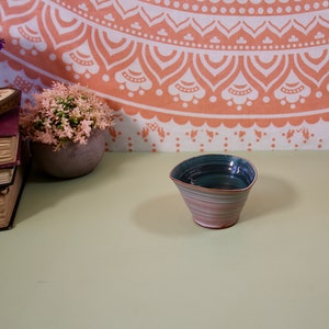 May include: A small, blue and pink ceramic bowl with a wavy rim. The bowl is sitting on a light green surface.