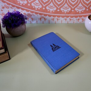 May include: A blue hardback book with a black silhouette of a building on the front cover.