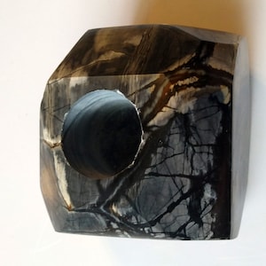 May include: A black and white stone sculpture with a circular hole in the center. The stone has a unique pattern of black and white veins.