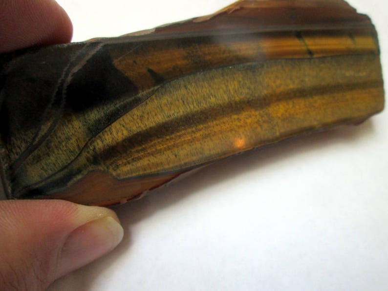 May include: A close-up of a tiger's eye gemstone with a brown, gold, and black color pattern. The gemstone has a smooth, polished surface.
