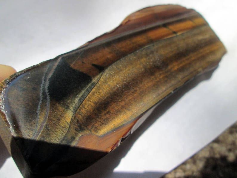 May include: A large, raw, brown and gold tiger's eye gemstone with a unique, banded pattern. The stone has a smooth, polished surface and is a natural, raw specimen.