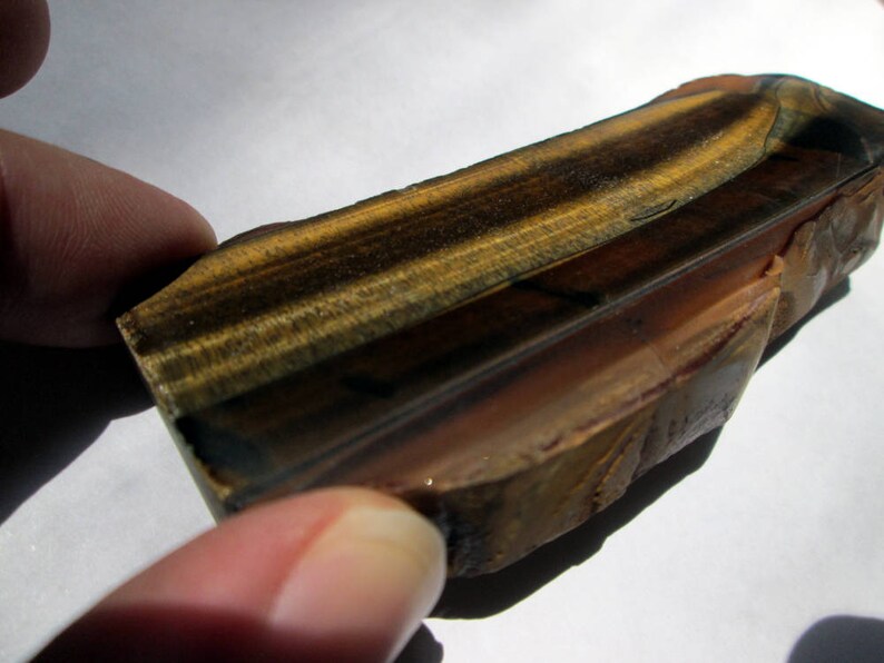 May include: A polished, rectangular piece of tiger's eye gemstone with brown, gold, and black stripes. The stone has a smooth, glossy finish.