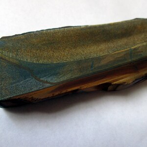 May include: A long, rectangular piece of polished stone with a blue and brown pattern. The stone has a rough, natural edge.