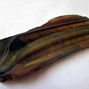 May include: A raw, unpolished piece of tiger's eye gemstone. The stone is a rich brown color with gold and black stripes. It has a natural, rough texture.