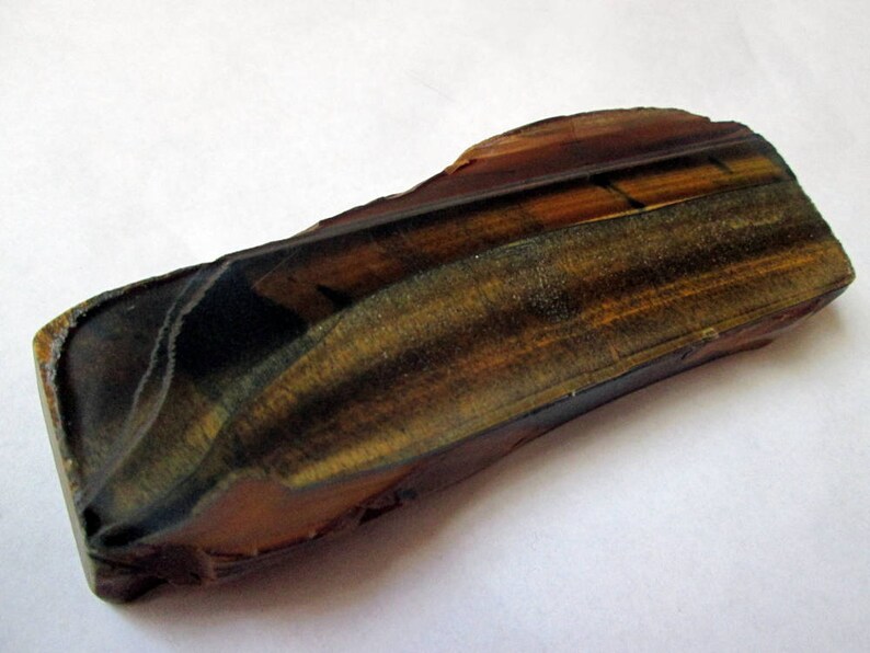 May include: A raw, unpolished piece of tiger's eye gemstone. The stone is a rich brown color with gold and black stripes. It has a natural, rough texture.