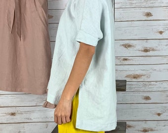 May include: A light blue linen top with short sleeves and a side slit. The top is loose fitting and has a relaxed silhouette.