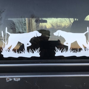 May include: White silhouette of two pointing dogs in a field of tall grass. The dogs are facing opposite directions and are in a hunting pose.