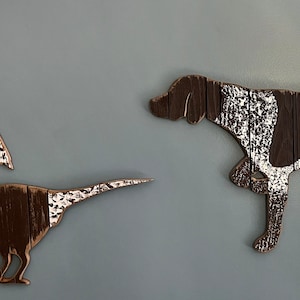 May include: Three wooden wall decor pieces in a rustic brown and white color scheme. The pieces are a German Shorthaired Pointer dog, a pheasant, and a pheasant in flight.
