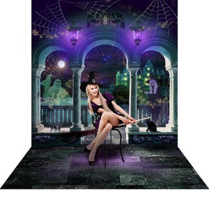 A Halloween photo backdrop featuring a stone balcony with arches, a glowing green castle, a ghost, a witch, a black cat, spiderwebs, and a woman in a witch costume sitting on a stool holding a broom.