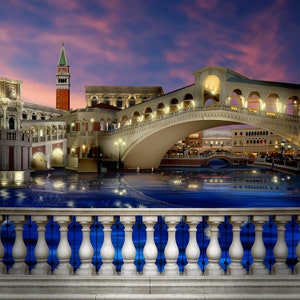 Puede incluir: Una vista de una r&eacute;plica de Venecia, Italia, con un puente sobre un canal. Los edificios est&aacute;n iluminados por la noche y el agua refleja las luces. Hay una barandilla de piedra blanca en primer plano.