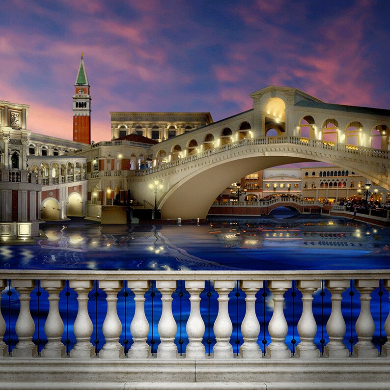 Puede incluir: Una vista de una r&eacute;plica de Venecia, Italia, con un puente sobre un canal. Los edificios est&aacute;n iluminados por la noche y el agua refleja las luces. Hay una barandilla de piedra blanca en primer plano.