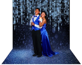May include: A couple in formal wear stands before a backdrop of shimmering lights. The man wears a blue waistcoat and bow tie with black trousers. The woman is in a long, royal blue gown. The background is dark blue with white lights.