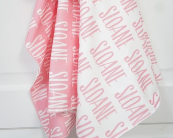 May include: A pink and white baby blanket with the name "Sloane" printed on it in white.