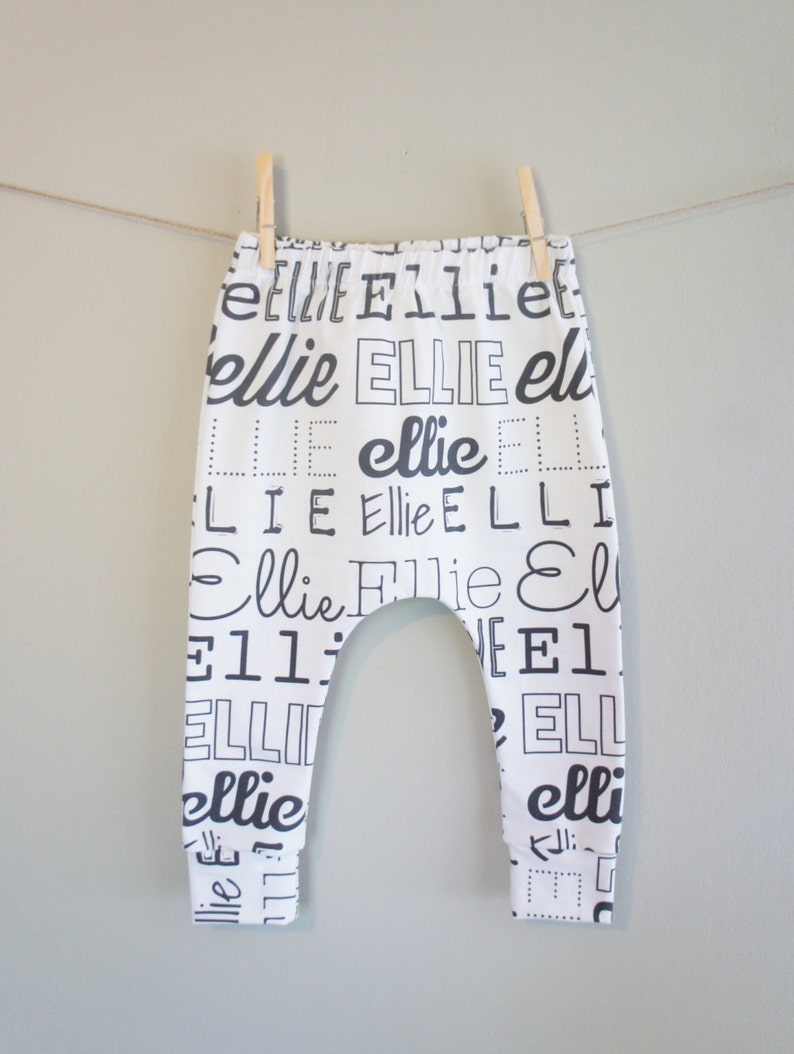 K&ouml;nnte beinhalten: Wei&szlig;e Baby-Leggings mit einem schwarz-wei&szlig;en Druck des Namens "Ellie", der in verschiedenen Schriftarten und Gr&ouml;&szlig;en wiederholt wird.