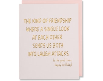 May include: A light pink and white card with gold foil lettering. The text reads "The kind of friendship where a single look at each other sends us both into laugh attacks. To the good times. Happy birthday!"