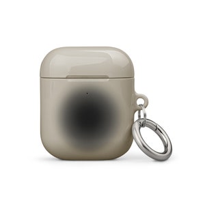 Puede incluir: Una funda de silicona beige con un diseño degradado negro para AirPods con un llavero de metal plateado.