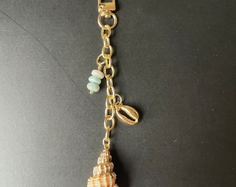 May include: Gold keychain with a seashell charm, blue beads, and a small gold seashell charm.