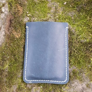 May include: A dark blue leather pouch with white stitching. The pouch is lying on a bed of green moss.