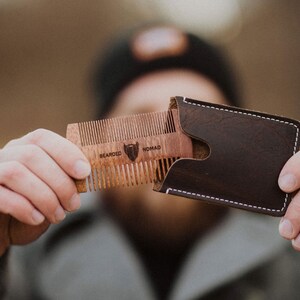 May include: A wooden beard comb with a leather case. The comb has the words "Bearded Nomad" engraved on it.