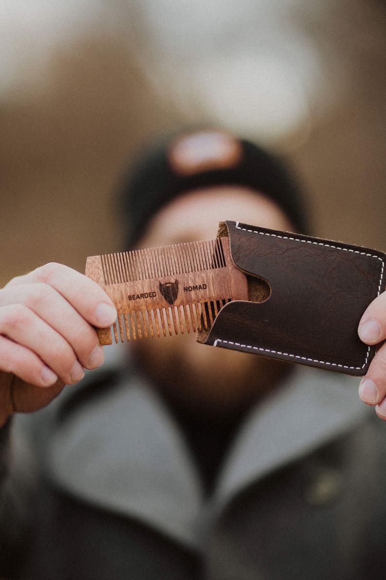 May include: A wooden beard comb with a leather case. The comb has the words "Bearded Nomad" engraved on it.