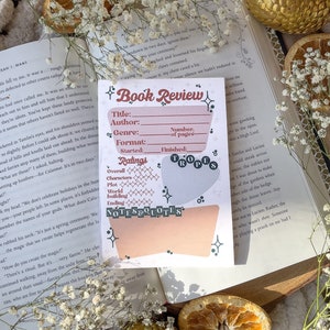 May include: A pink and white printable book review tracker with a whimsical design. The tracker includes sections for title, author, genre, format, started, finished, number of pages, ratings, notes, and quotes. The tracker is decorated with stars, hearts, and a floral pattern.