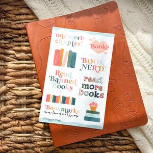 May include: A set of colorful book-themed stickers with text that reads "one more chapter", "Books", "Book Nerd", "Read Banned Books", "read more books", and "Bookmarks are for quitters Meaggie Moos".