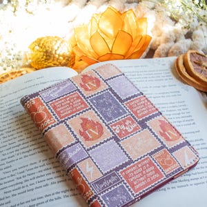 May include: A book cover with a patchwork design of postage stamp-like squares in shades of orange, purple, and red. The squares feature illustrations and text, including the words "Oranges" and "A Dragon Without Its Rider Is A Tragedy". The cover is open on a book.