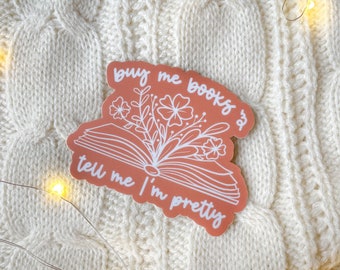 May include: A pink sticker with a white outline of an open book with flowers and the text "buy me books & tell me I'm pretty".