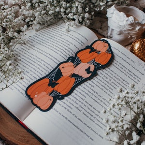 May include: A book with a black and orange pumpkin bookmark. The bookmark features a spider web design and a small butterfly.
