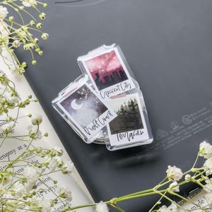 Puede incluir: Imanes transparentes de estilo Polaroid de acrílico con arte de paisajes y texto. Los imanes presentan imágenes de un cielo nocturno, un paisaje urbano y un bosque. El texto incluye "Night Court", "Crescent City" y "Terrasen".