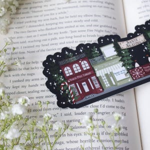 May include: A black and white sticker with a Christmas theme. The sticker features a red building with the words "North Pole Library" and "Books" on it. There are also two other buildings, one with the words "Toy Workshop" and the other with the words "Santa Skating".