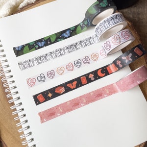 K&ouml;nnte beinhalten: Sortiment von sechs dekorativen Washi-B&auml;ndern mit verschiedenen Designs, darunter Schmetterlinge, Herzen, B&uuml;cher und Sterne. Die B&auml;nder befinden sich auf einem wei&szlig;en Hintergrund.