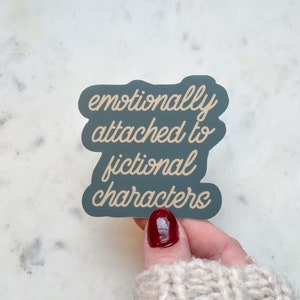 May include: A teal blue sticker with the text "emotionally attached to fictional characters" in a beige script font.