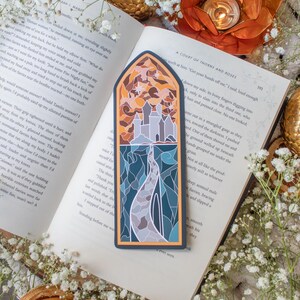 Pu&ograve; includere: Un segnalibro in vetro colorato che presenta un sentiero tortuoso che conduce a un castello con un bagliore dorato. Il segnalibro &egrave; posizionato su un libro con il testo "A Court of Thorns and Roses".