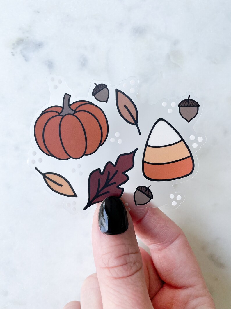 Puede incluir: Una hoja de pegatinas transparente con ilustraciones de tem&aacute;tica oto&ntilde;al. La hoja incluye una calabaza, un caramelo de ma&iacute;z, bellotas y hojas en tonos naranja, marr&oacute;n y rojo.