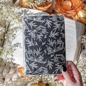 Puede incluir: Una funda transparente para teléfono con fondo negro y un diseño blanco de libros y hojas.