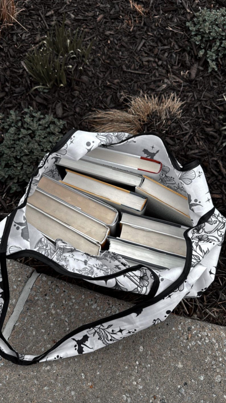 Peut inclure: Un sac fourre-tout blanc avec un motif floral noir et une fermeture &eacute;clair noire. Le sac est rempli de plusieurs livres reli&eacute;s.