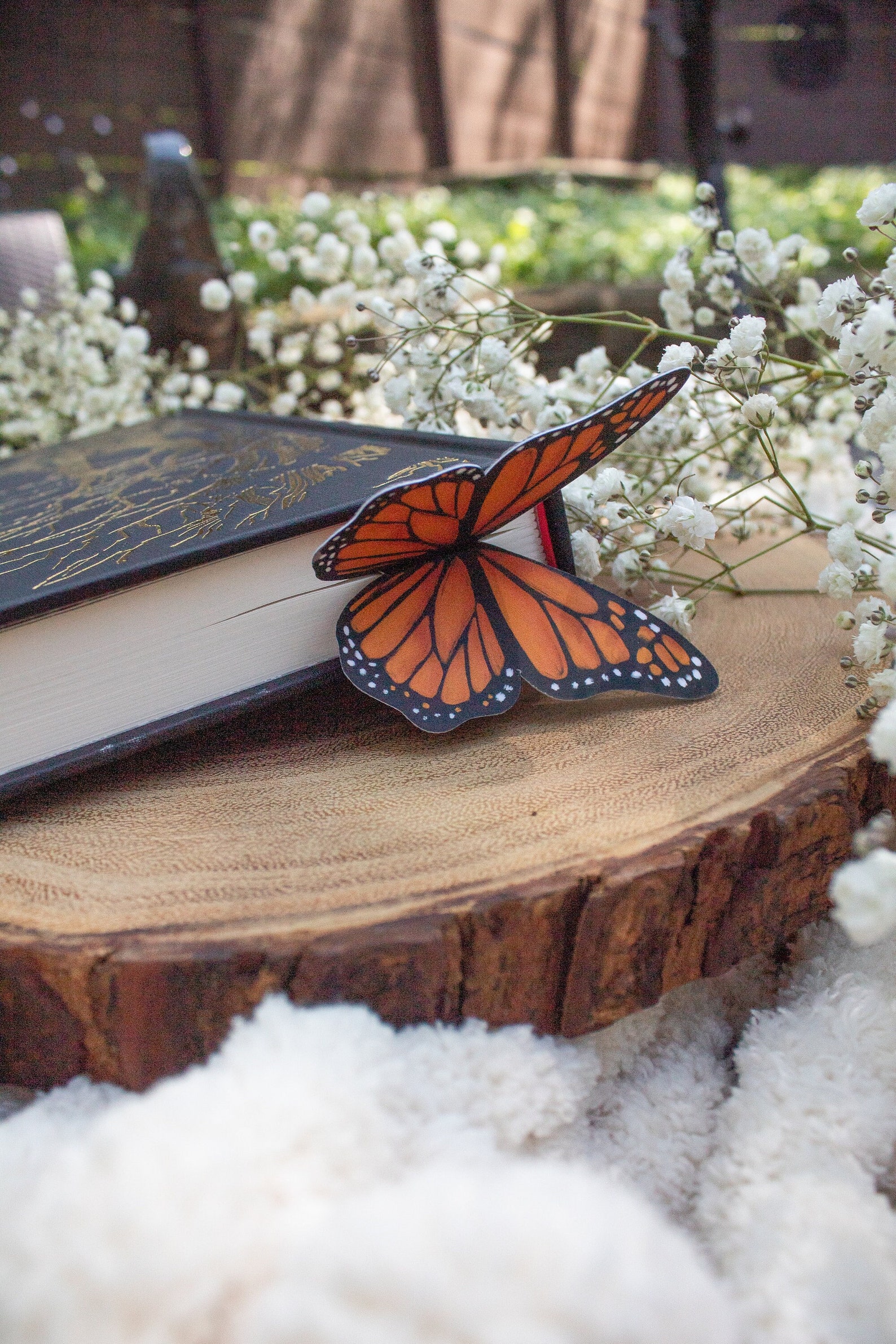 A thick paper butterfly on top of a book's pages, connected to a bookmark, sitting on a wooden plate.