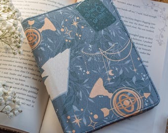 May include: A blue book cover with a gold and white design featuring stars, moons, and a compass. The text "A Court of Thorns and Roses" is visible on the cover.
