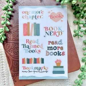 May include: A sheet of stickers with a book theme. The stickers feature illustrations of books, hearts, and text that says "one more chapter", "Books", "Book Nerd", "Read Banned Books", "read more books", and "Bookmarks are for quitters".