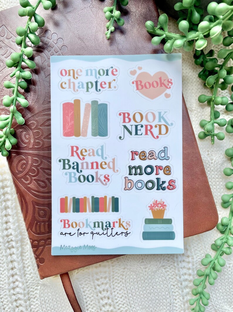 May include: A sheet of stickers with a book theme. The stickers feature illustrations of books, hearts, and text that says "one more chapter", "Books", "Book Nerd", "Read Banned Books", "read more books", and "Bookmarks are for quitters".