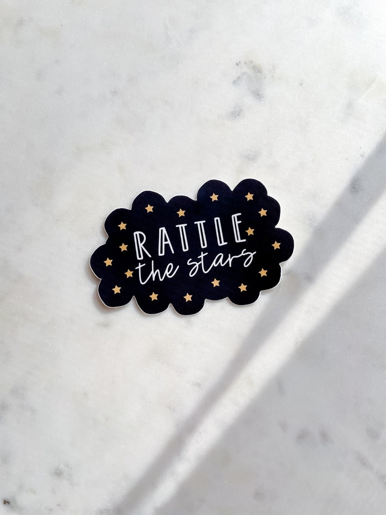 Peut inclure: Autocollant noir et blanc en forme de nuage avec des &eacute;toiles dor&eacute;es. Le texte "Rattle the stars" est &eacute;crit en blanc.