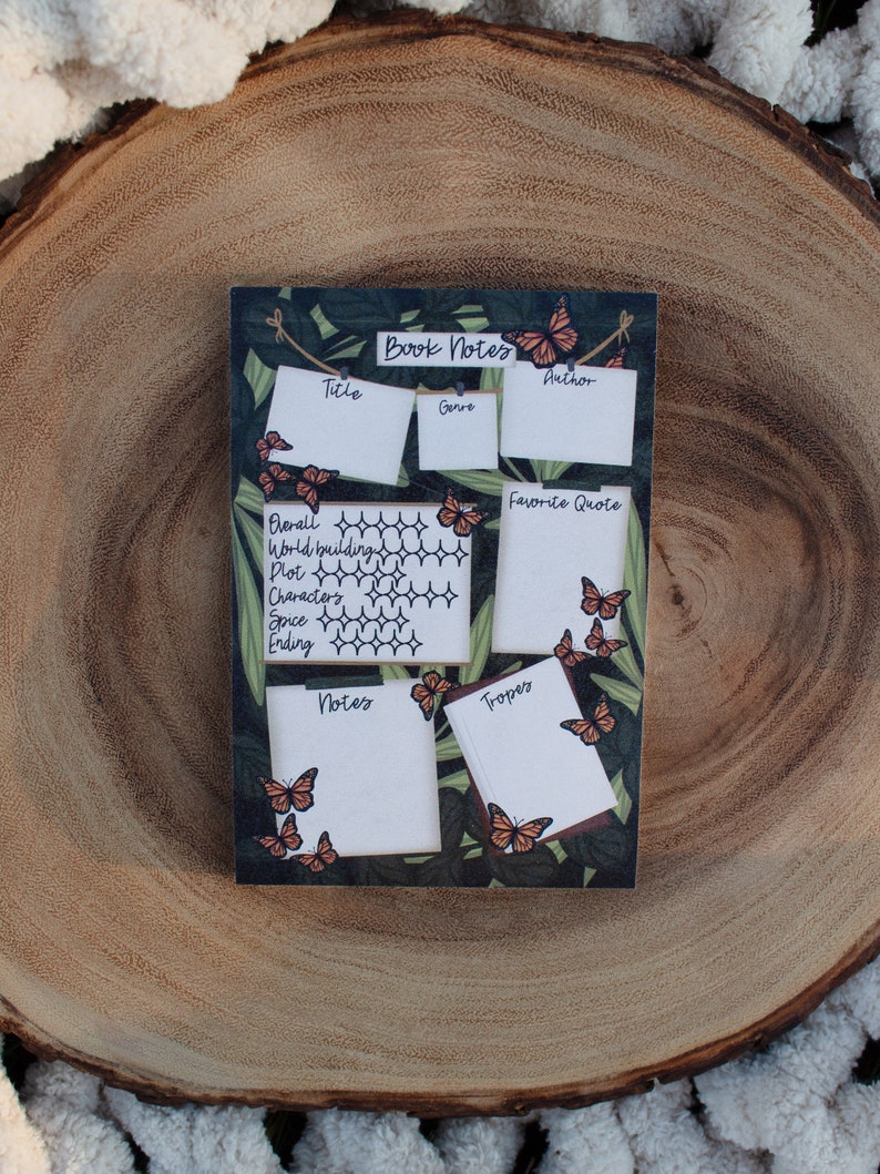 K&ouml;nnte beinhalten: Eine rechteckige Notiztafel f&uuml;r B&uuml;cher mit dunkelgr&uuml;nem Hintergrund und Schmetterlingsakzenten. Die Tafel hat Abschnitte f&uuml;r Titel, Genre, Autor, Lieblingszitat und Notizen. Die Tafel ist mit orangefarbenen Schmetterlingen verziert.