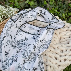 Peut inclure: Un sac de courses r&eacute;utilisable blanc avec un imprim&eacute; noir et blanc de chauves-souris, de fleurs et d'autres motifs d'inspiration gothique. Le sac est fait d'un mat&eacute;riau fin et translucide et a une bordure noire.