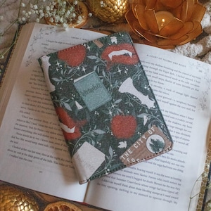 May include: A green and red book cover with a floral pattern and the words "The City of  For" on the front. The book cover is lying open on a book with the title "A Court of Thorns and Roses".